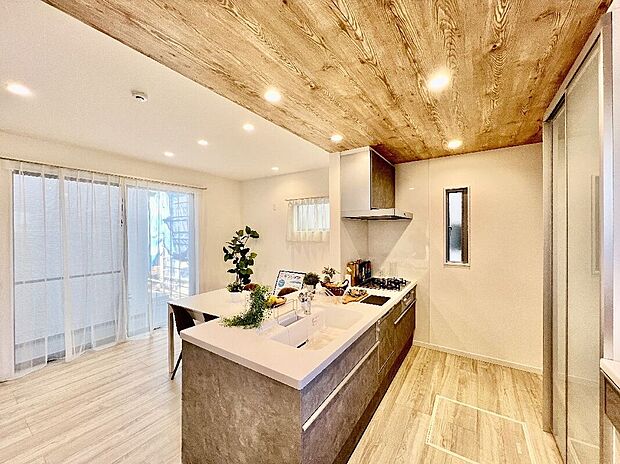 【【キッチン/施工例】】ホワイトの人造大理石のワークトップにより、明るく清潔感を感じられるシステムキッチンはLIXIL製。上部は、フロアとは異なるトーンの木目があたたかみを添える折下天井に。