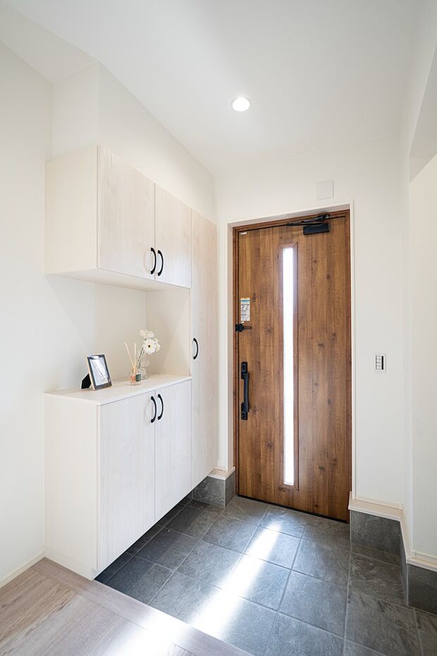 【【1階玄関/B号地】】スリットガラスから自然光が伸びやかに届くエントランス。コの字型の玄関収納と向かい合わせで土間収納を配置しており、ベビーカーやお子様の外遊びのおもちゃなども保管いただけます。