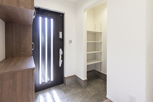 【【1階玄関/C号地】】ス自然光が注ぎ込む玄関ドアはポケットキー付きで、施開錠がスムーズに行えます。玄関収納と土間収納を向かいあわせに配置し、靴だけでなくアウトドア用品なども汚れを邸内に持ち込まずに保管いただけます。