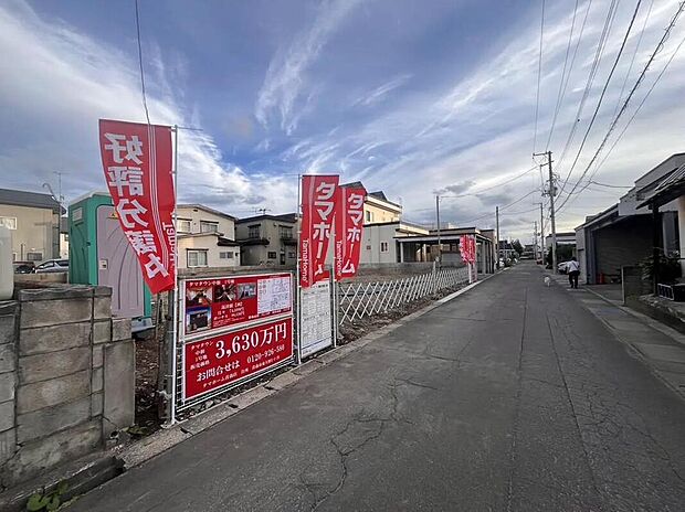 現地外観写真:前面道路は幅約4mの静かな住宅街に面し、区画は整備済みでタマホームの赤い幟や3,630万円の案内看板が確認でき、生活利便性の高い落ち着いた住環境を感じさせます。