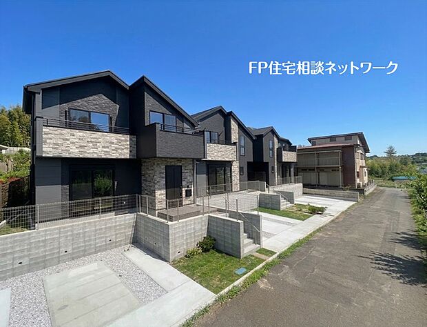 【外観】  黒と石目調のモダンな外観が印象的な、全4棟のスタイリッシュな新築分譲住宅。開放感あふれるワイドバルコニーや充実の駐車スペースを完備。青空に映える美しい住まい。