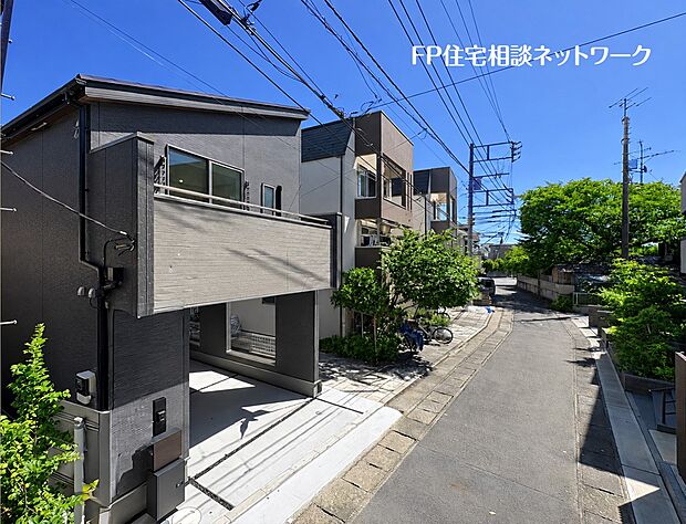 【外観】  現地周辺は戸建住宅が建ち並ぶ、落ち着いた街並み。沿道の豊かな緑と鮮やかな青空が住まいを引き立てます。建物の外観と前面道路の様子をあわせてご確認いただける一枚です。