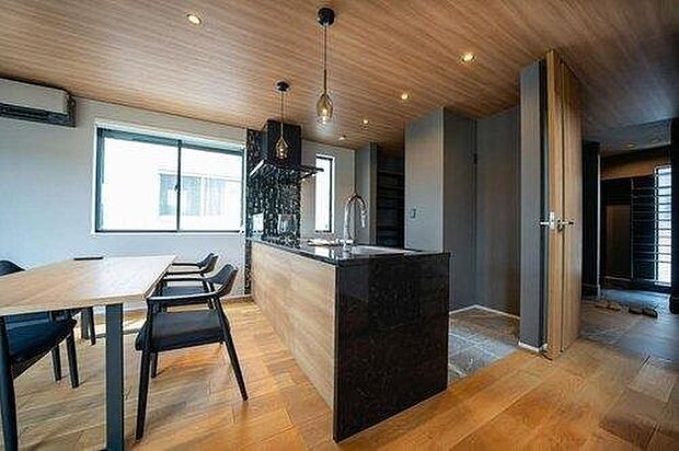 【内観】【建物プラン例　建物価格2100万円、建物面積100m2】木の温もりとブラックキッチンの洗練が融合。上質な素材感と落ち着いた照明が、心地よい大人の空間を演出します。