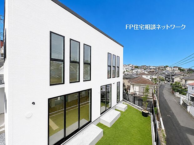 【庭】【外観│庭】 青空に映える白を基調としたスタイリッシュな外観。規則正しく並んだ黒枠の窓と大きな開口部がアクセントとなり、モダンな雰囲気を演出しています。