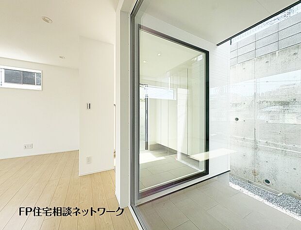 【その他内観】【中庭】 室内から望む、明るい光が差し込む玄関土間スペース。ガラス越しに見えるコンクリートの打ちっぱなしの壁が、シンプルで洗練された空間を演出しています。雨の日でも快適なインナーガレージへの動線も魅