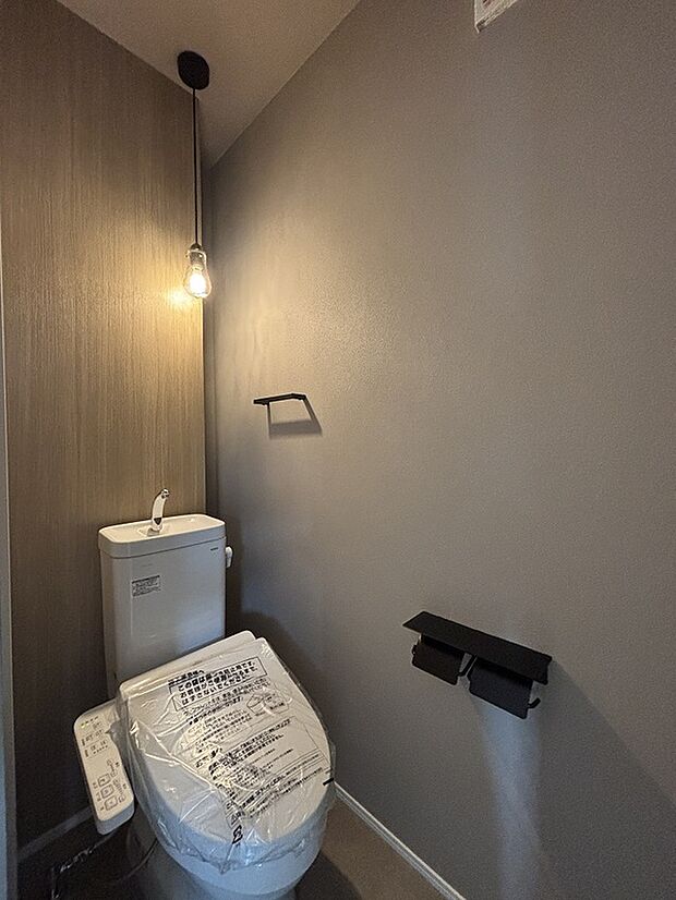 【2階トイレ】夜に使うことが多い2階のトイレはグレーのクロスとペンダントライトで明るすぎず、落ち着けます。トイレの背面には掃除道具やトイレットペーパーのストックが置けます。
