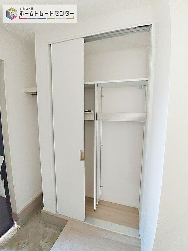 【玄関脇のスライド扉収納】スライド扉の玄関収納。内部に棚とハンガーパイプを備え、靴や上着の収納に便利な造りです。明るい白系の内装。
