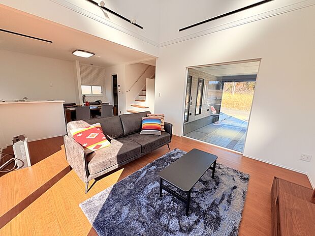 【1号棟　LDK】吹き抜けが開放感を演出する18.5帖のLDK 。リビングの大きな窓から愛車を眺める、贅沢なガレージライフを実現しました。趣味と家族の時間が心地よくつながる住まいです。