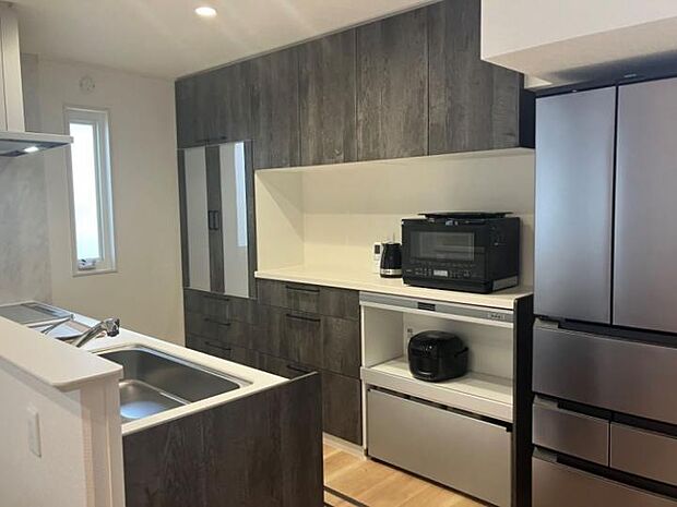 【キッチン】背面には食器棚と家電収納を配置。カウンター下はゴミ箱が入るワゴン収納付。(2025年10月撮影)