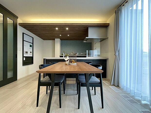 木目調の下がり天井とやさしく灯る間接照明が、ダイニングを心地よく演出。奥のタイル調キッチンとも調和し、何気ない毎日を少し特別に感じられる空間です。