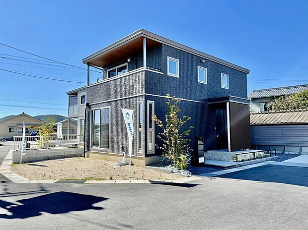 【3号地外観】深みのあるダークトーンの外観が印象的な、落ち着きある佇まい。玄関まわりの木調アクセントがやさしい温もりを添え、街並みに上品になじむ住まいです。