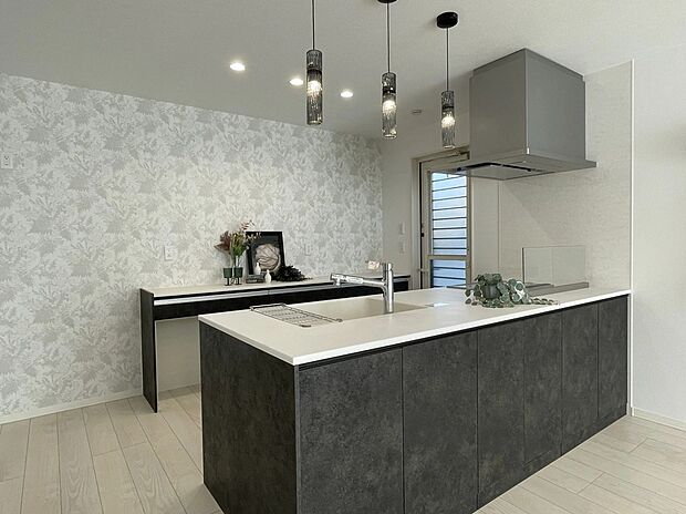 【1号地 キッチン】背面のボタニカル柄クロスが空間を華やかに彩るキッチン。ダークトーンのパネルと調和し、落ち着きある雰囲気に仕上がっています。毎日の料理が楽しくなる、こだわりの空間です。