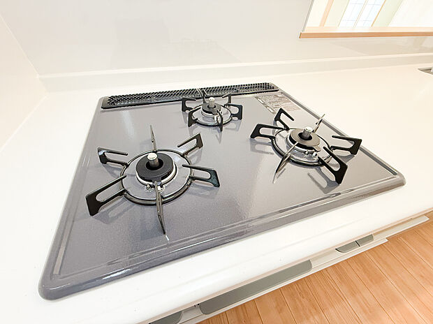 【ー三口コンロー】(B号棟)ガスコンロ採用のキッチンは、火力のコントロールがしやすく料理好きの方にも最適な設備です。本格的な調理を思う存分楽しめる充実した調理環境が整っています。