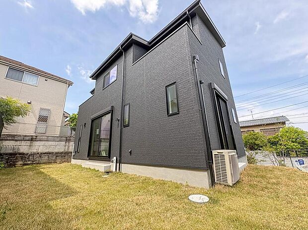 【現地外観写真】洗練されたダークトーンの外観が印象的な住まい。広々とした庭は、お子様とのびのび遊べる家族の憩いの場です。
