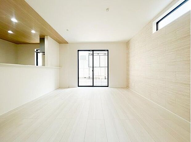 【リビング】広々とした15帖のLDKは、白を基調とした明るく開放的な空間。天井の木目調アクセントとダウンライトが、都会的でありながら温かみのある雰囲気を演出します。家族が自然と集まる、心地よいリビング。