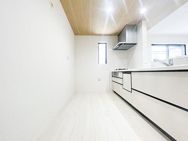 【キッチン】天井に施された木目調のアクセントクロスとダウンライトが、カフェのような上質な空間を演出します。対面式キッチンなので、お料理中もリビングで過ごすご家族や、宿題をするお子様と会話が弾みます。