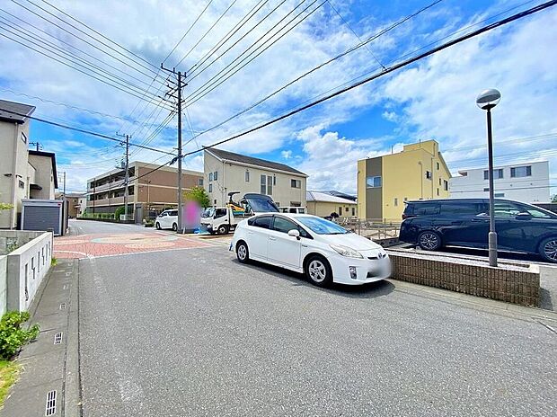 【前面道路と敷地周辺の外観】前面道路(幅員約6m、アスファルト舗装・交差部はインターロック)越しに敷地周辺の住宅景観が確認できます。敷地は駐車2台想定のゆとりある広さです。現地(2026年8月)撮影