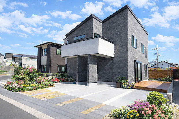 【外観施工例】重厚なグレー外壁と迫力のバルコニー、開放的なウッドデッキが魅力の邸宅。
