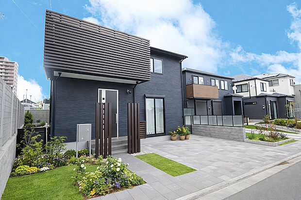 【施工例外観】ダークトーンの外壁と水平ラインが美しく映える、洗練されたモダンデザインの住まい。ゆとりあるカースペースと整えられた外構計画が上質な印象を演出し、街並みに調和しながらも存在感を放つ一邸です。