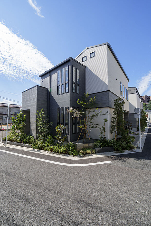 【３号棟（2026年9月撮影）】道路角に建つ木造2階建ての外観。ツートンの外壁と縦長窓、植栽が配され、舗装道路に面しています。