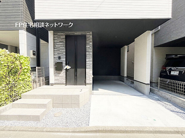 【モダンな玄関アプローチ】石目調のアクセント壁とシックな黒いドアが目を惹く、高級感あふれるエントランス。深いビルトインガレージは愛車を守るだけでなく、雨の日でも濡れずに玄関へアクセスできる便利な動線が魅力的なお住まいです。