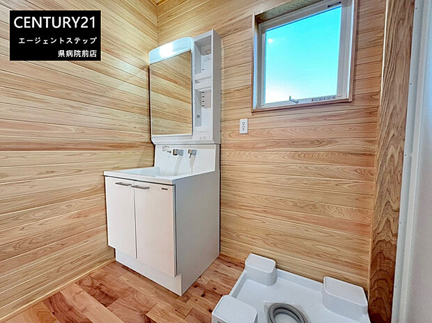木目調の壁が印象的な洗面所です。窓付きで換気しやすく明るい空間です。シンプルな洗面台でお手入れも簡単です。収納スペースも確保されています。