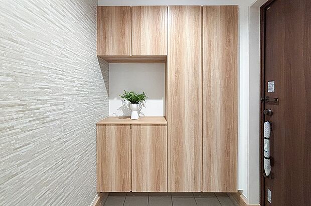 【玄関】温かみのある木目調の収納と、質感豊かなアクセントウォールが上質な空間を演出します。毎日の外出や帰宅が楽しみになる、住まいの顔にふさわしい玄関です 。(1号棟)