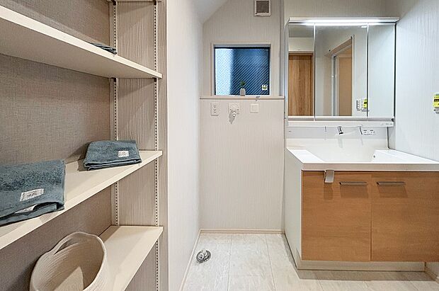 【洗面台・洗面所】洗面台横には便利な可動棚を設置。バスタオルやパジャマ、洗剤のストックなど、すぐ近くにたっぷりと収納できます。棚板の高さは自由に変えられるため、無駄なくスペースを活用できるのが魅力です 。(1号棟)