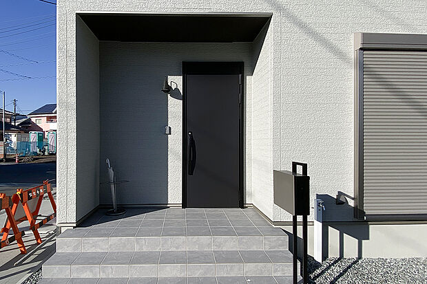 【雨の日も安心の奥行きある玄関ポーチ】奥行きのある玄関ポーチが雨の日の出入りを快適にサポート。シンプルで上質な玄関ドアと外壁が、住まいの印象をさらに引き立てます。
