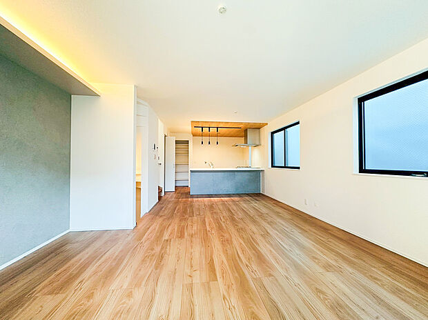 広々としたリビングダイニングは、明るいフローリングと白壁を基調とし、空間の広がりを感じさせます。壁際の間接照明と、モダンなアクセントクロスが落ち着いた雰囲気を演出。