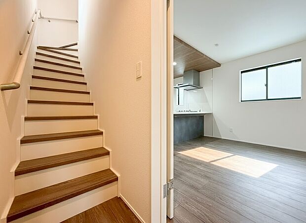階段室からリビングへ一歩足を踏み入れると温かみのある木目調のフローリングと陽光を美しく反射する白い壁面が広がる開放的な空間が迎えてくれます。キッチンへと続くスムーズな動線は家族の気配を常に感じられます