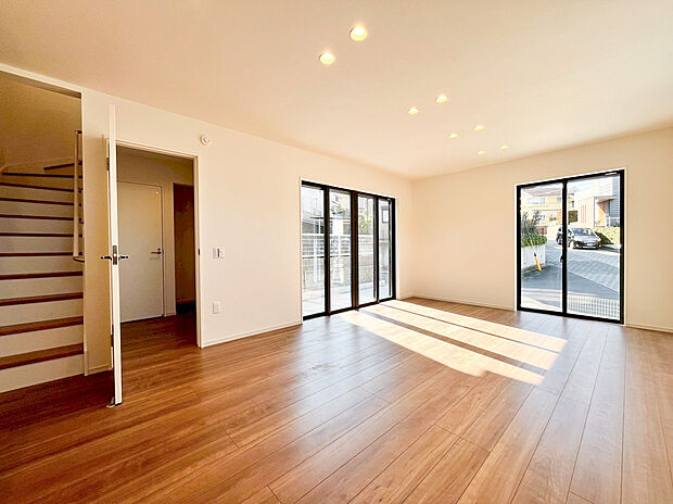 【リビング】ダウンライトを配したモダンな天井と、光を反射する明るいフローリングが、空間の広がりをさらに強調します 。南西向きのワイドな開口部からは、遮るもののない陽光が室内の隅々まで届きます。