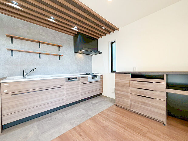 【キッチン】木目調とグレーのアクセントクロスや木ルーバー調の天井がおしゃれな雰囲気を演出します。食洗機付きのシステムキッチンは、デザイン棚がカフェのような空間に。