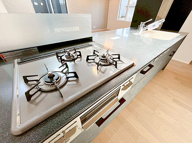 【システムキッチン】お手入れ簡単なガラストップコンロを搭載し、家事の時短に貢献します。ダークグレーの石目調カウンターは見た目にも美しく、毎日の調理を快適にする、こだわりの設備です。