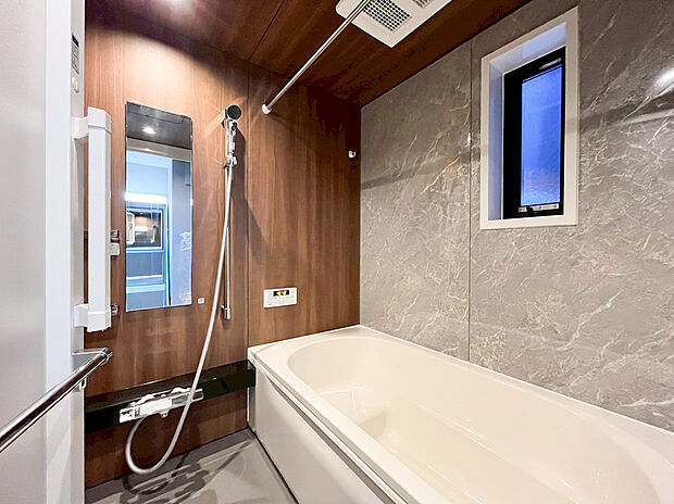 【ユニットバス】木目調のアクセントパネルと石目調の壁面が調和した、高級感あふれる癒しのバスルームです。ゆったりとした浴槽は、一日の疲れを解きほぐす至福のバスタイムを演出します。