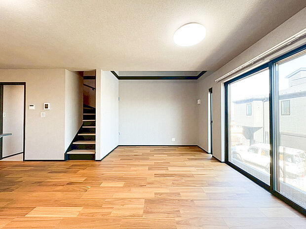 【リビング】南向きの大きな開口部から陽光がたっぷりと差し込み、日中の大半を照明なしで心地よく過ごせるリビングです。落ち着いた色合いのアクセントクロスと、ぬくもり溢れる木目調のフローリングが、安らげる空間を演出。