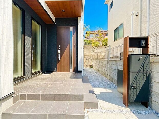 【宅配ボックス】モダンで落ち着いた色調が印象的な玄関アプローチは、住まいの顔として上質な品格を演出しています。また、不在時にも重宝する宅配ボックス付きの機能門柱を完備しており、共働き世帯にも嬉しい仕様となっています。