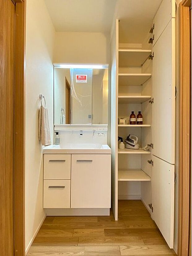 【洗面台】三面鏡付きの洗面化粧台。三面鏡の裏側やシンク下も収納たっぷり。引き出し収納は奥の物も取り出しやすく、観音開きの方には高さのあるものも置けます。また可動棚タイプの収納も設置。タオル類や洗濯用品の収納にも