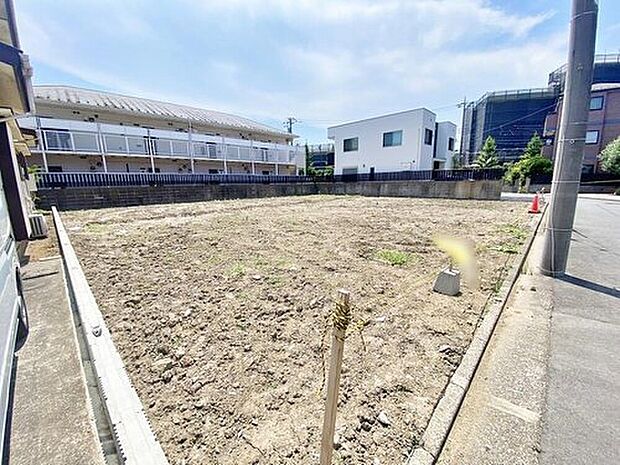 【現地外観写真】現地(2026年7月)撮影。整地された平坦な更地です。前面道路に面しており、周囲に戸建てや集合住宅が確認できます。