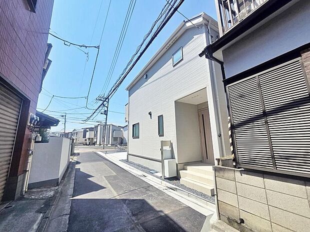 【前面道路含む現地写真】現地(2026年8月)撮影
白い2階建ての外観写真。玄関ポーチと郵便受けが確認でき、舗装された公道に面しています。隣家が近接する街並みです。