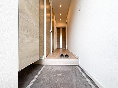 ナチュラルな木目調扉とスタイリッシュな土間タイルが調和する上品な玄関。ダウンライトの温かな光が奥行き感を演出し、来客時にも洗練された上質な第一印象を与えます。