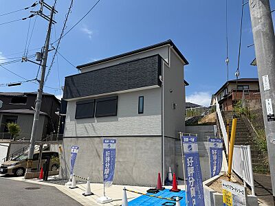 外観：明るい日差しの下、爽やかな外観の新築戸建て。落ち着いたグレーの外壁が周辺環境に調和し、暮らしやすい環境が広がります。