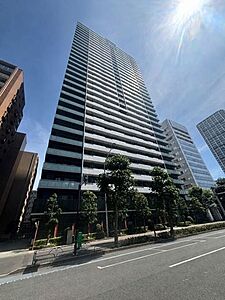 外観：白とダークカラーを基調としたスタイリッシュな外観デザインの高層マンションで、バルコニーには透明感のある手すりが施されており、前面道路沿いには緑豊かな街路樹や植栽が整えられています。