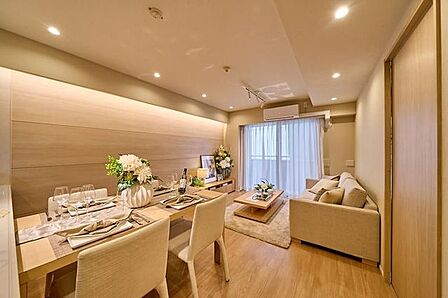 ナチュラルな質感の木目調フローリングが施工された居室には、壁面に間接照明と木目調アクセントパネルが施されており、天井には複数のダウンライトやエアコン、バルコニーへ出られる開口部が備わっています。