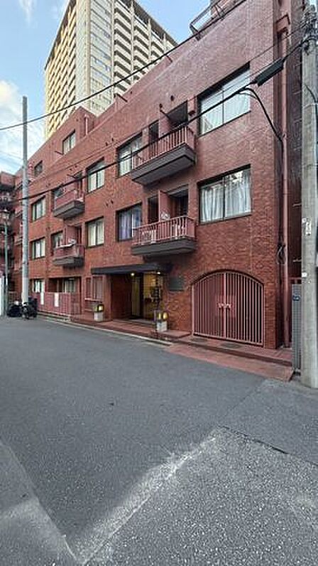 温かみのある赤茶色のタイル貼り仕上げの外観デザインで、各住戸にバルコニーや大きな窓が備えられており、舗装された前面道路から階段とスロープを通ってエントランスへアプローチする造りとなっています。