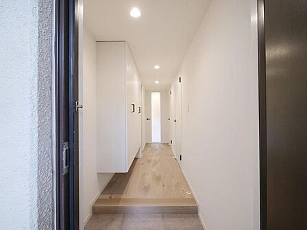 白を基調とした壁と木目調のフローリングが特長的な玄関には、足元に空間のあるフロートタイプのシューズボックスが備え付けられており、廊下の正面にはスリットガラスが入ったドアが配されています。