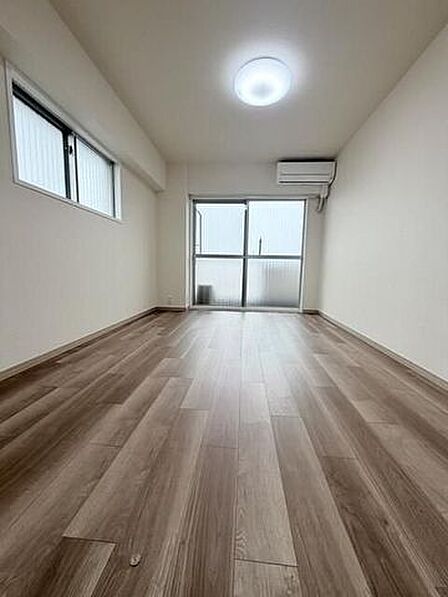 落ち着いた木目調のフローリングと白いクロスで仕上げられた洋室で、正面と側面の2方向に窓が設置されているほか、エアコンと天井照明設備が備え付けられています。