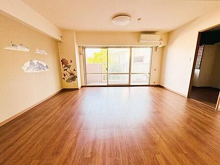 木目調のフローリングが採用された洋室には、バルコニー側に向いた大きめのガラスサッシや天井照明、エアコンが設置されており、白を基調とした壁面にはワンポイントのステッカーが施されています。