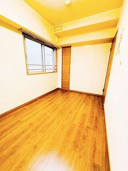 ナチュラルな木目調フローリングと白い壁紙で構成された洋室には、手すり付きの腰高窓が配置されており、部屋の奥と右側の2箇所に木目調のデザイン扉が備え付けられています。
