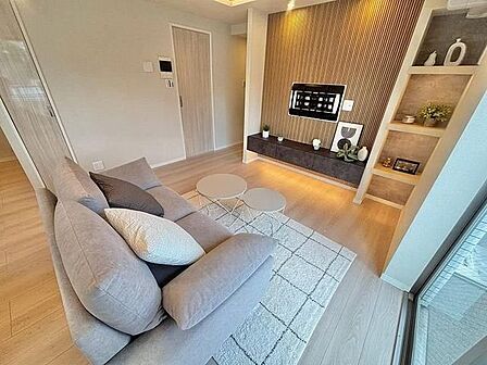 木目調アクセントパネルや壁掛けテレビ用金具を備えた室内に、足元照明付きのフロートボードや作り付けの飾り棚を設置し、ナチュラルな木目調のフローリングや建具で統一感のある設えとなっています。